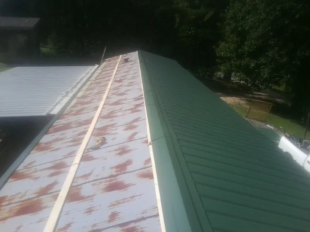 Old rusted panels beside newly installed green metal roofing — Wind Damage Roof Repair by Roofing Brothers in Church Point
