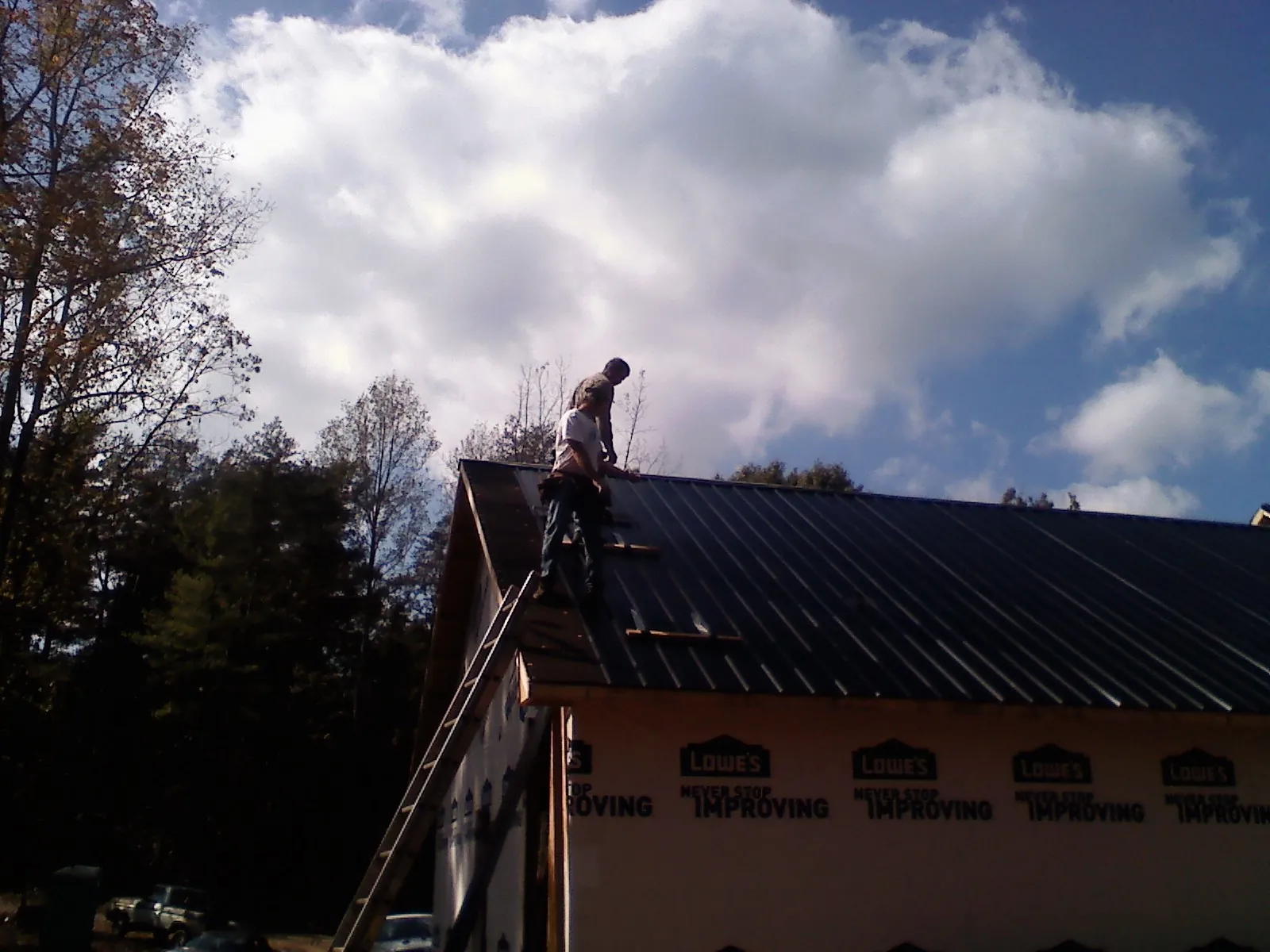 Roofer fastening dark metal panels high against a cloudy sky, from a Roof Inspection job in Church Point