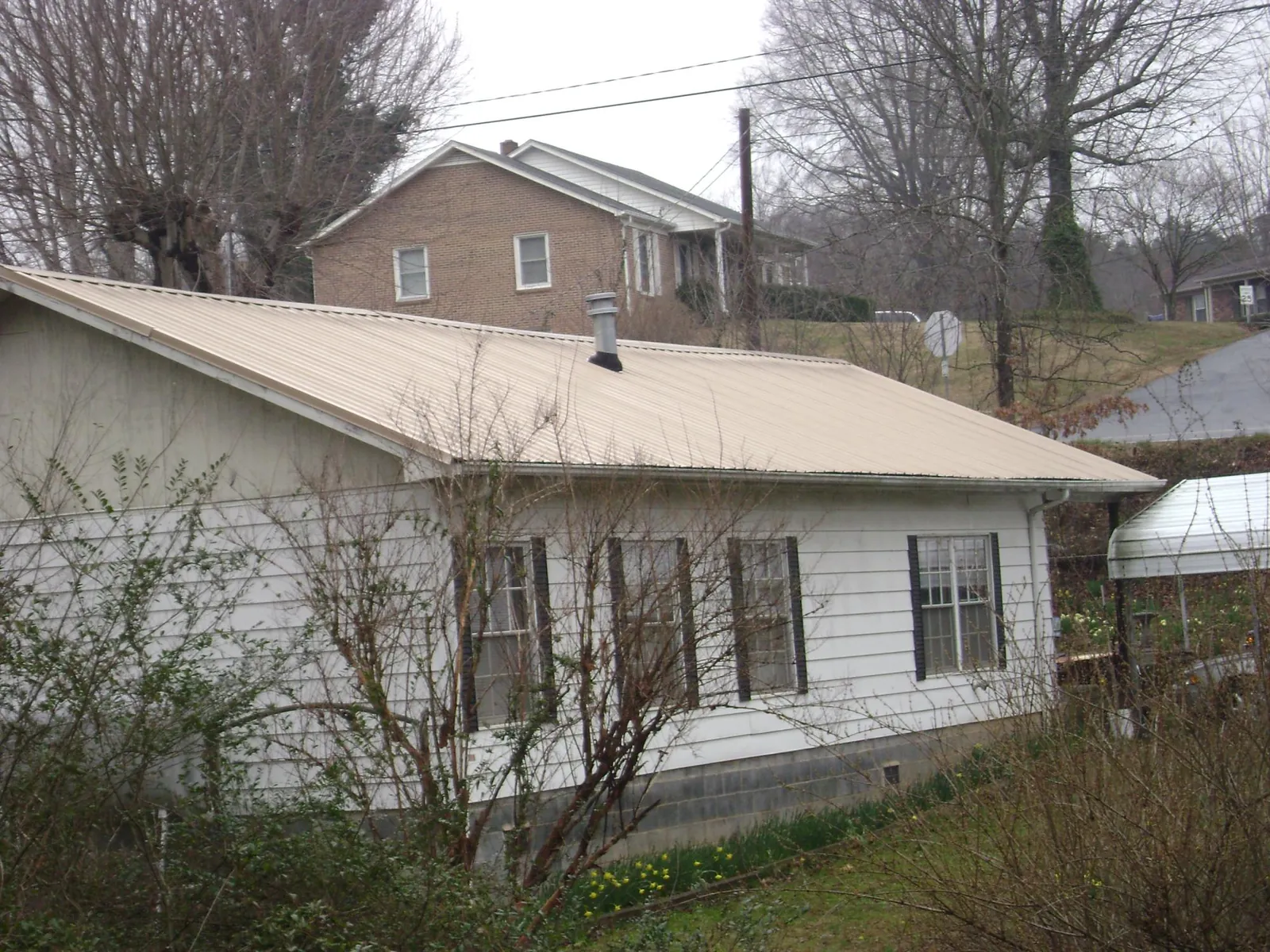 Tan metal roof on a white sided house set into a hillside — Commercial Roofing by Roofing Brothers in Church Point