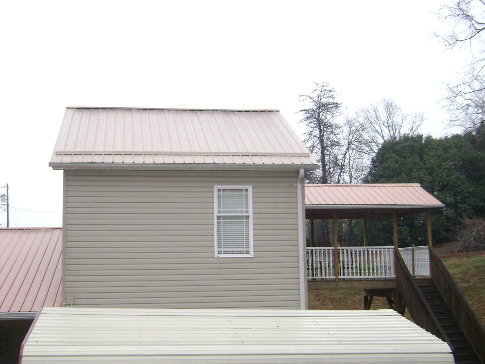 Tan metal roofs on a two story addition and attached porch, from a Roof Replacement job in Church Point
